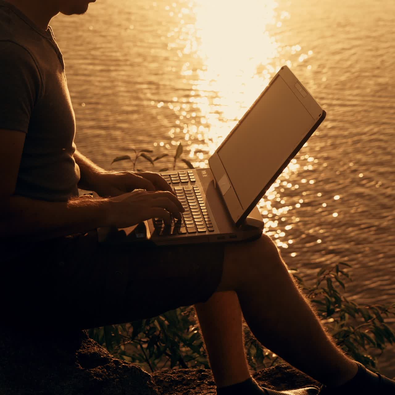 Giovane uomo d'affari che lavora al laptop al tramonto. Lavoro freelance online, focus sullo schermo.