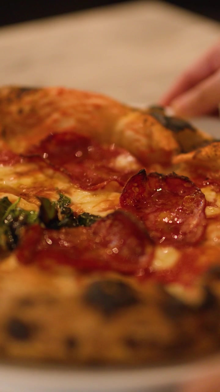 Primo piano di una mano che afferra una fetta di pizza al lievito madre con salame piccante in un ristorante