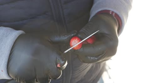 primer plano de manos con guantes negros cortando una fresa