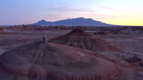 Drone-flying-over-man-walking-in-colourful-rock-formations-at-Mars-desert-research-station-in-Utah,-United-States