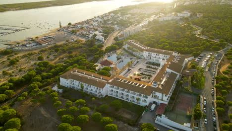 aerial orbiting around garden playanatural hotel and spa surrounded with stone pine forest and coastline of piedras river and marina el rompido port under sunset light, spain