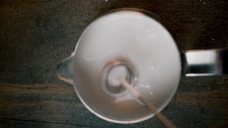 top view coffee creamer with electric milk frother stick coming out and mixed milk bubbling on dark background