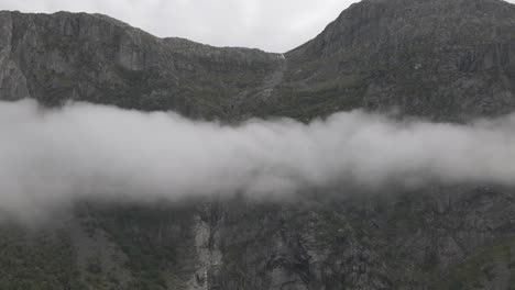 rocky mountain range above fluffy cloudscape, aerial pan right shot