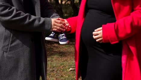 pregnant couple outdoors holding baby shoes and touching belly in loving anticipation