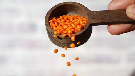 red lentils pouring from a wooden spoon