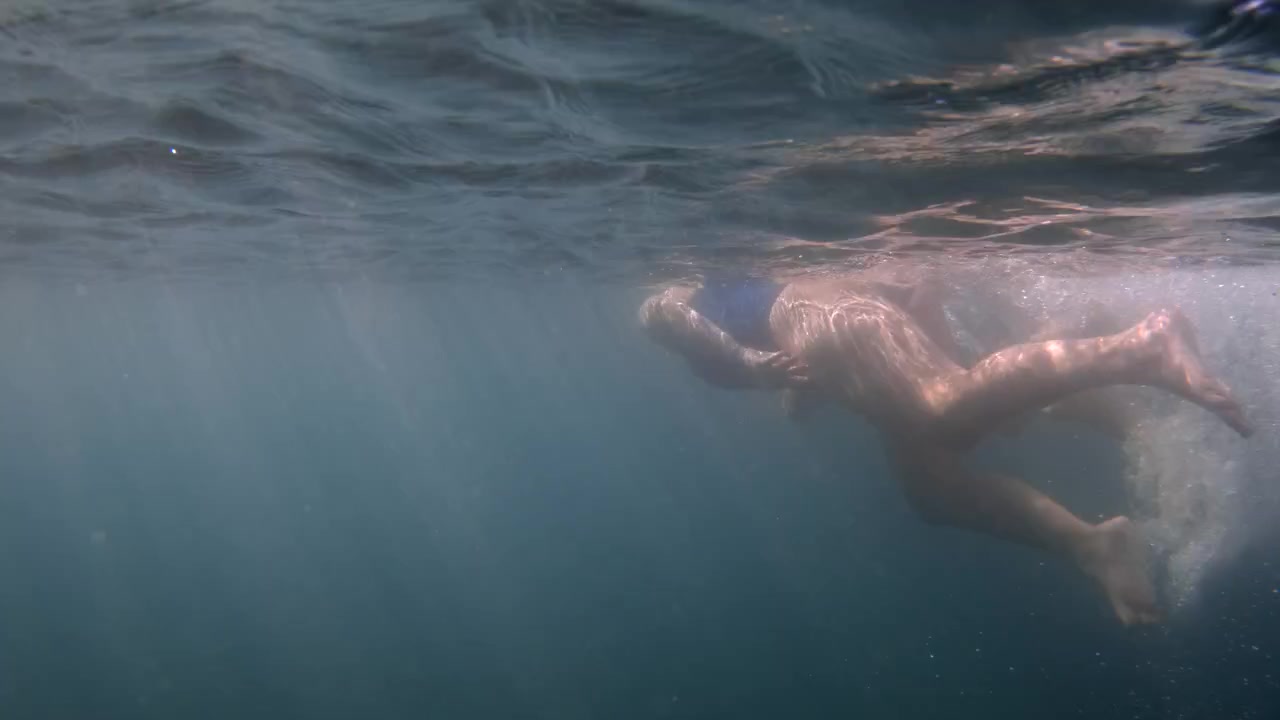 Mujer disfrutando de un refrescante baño en agua clara y azul del océano. La luz del sol filtrándose a través de la superficie crea una belleza submarina natural.