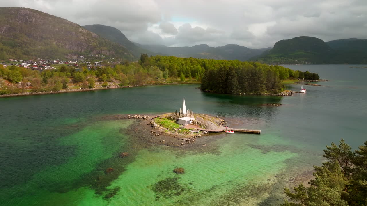 Ilmakuva Solspeilet-kivimonumentista pienellä rannikkosaarella lähellä Jørpelandia, Norjassa. Monumenttia ympäröi turkoosi vesi, metsä ja kaukaiset vuoret.