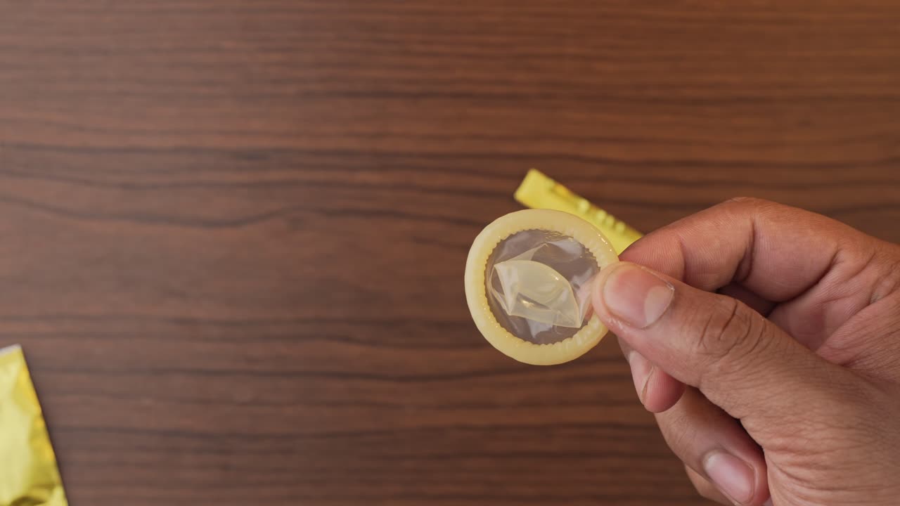 Persona che apre una confezione di preservativi con le dita e mostra un preservativo