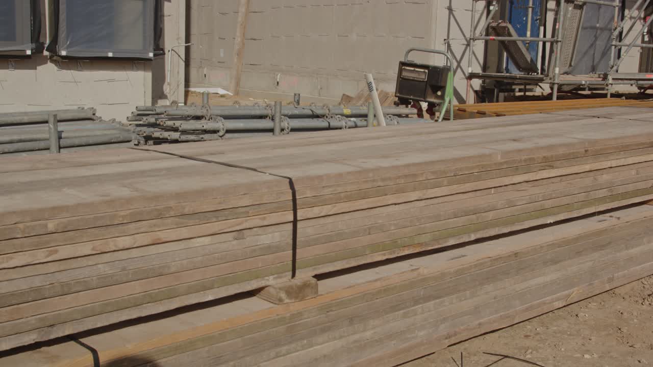 Wide pan of wooden walkboards stacked and tied up on a construction site on a sunny day