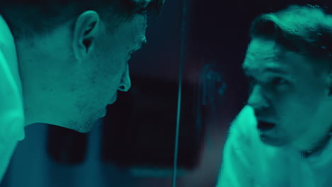 Man in distress looking into a mirror at night.