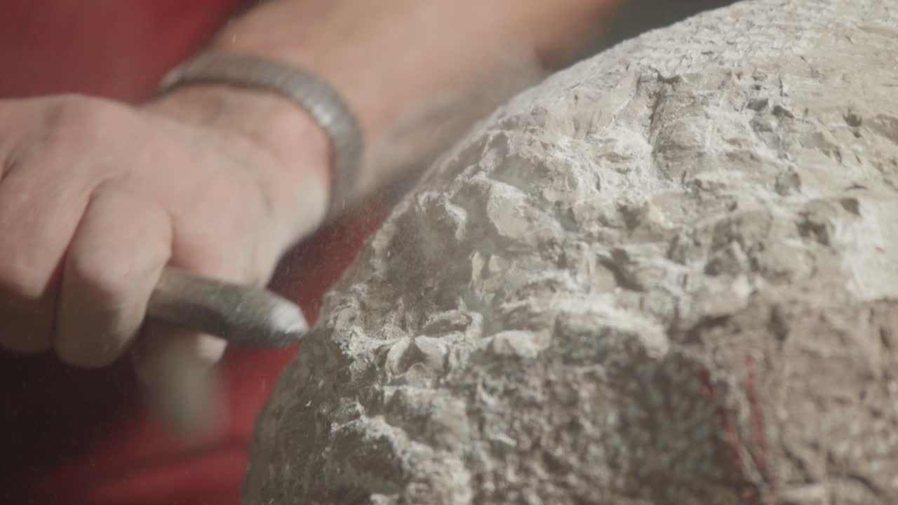 vista de cerca sobre el momento de la talla artística de piedra con un hombre y su herramienta de martillo, italia.