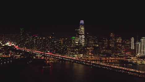 Toma-Aérea-De-Los-Rascacielos-De-San-Francisco-Desde-El-Puente-De-La-Bahía-Por-La-Noche