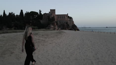 Disparo-De-Un-Dron-Siguiendo-A-Una-Chica-Tatuada-Hasta-El-Castillo-De-La-Playa-En-Lisboa,-Portugal