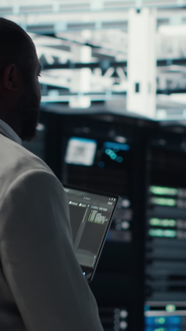 Vertical video Engineer walking in server farm, automating system diagnostics