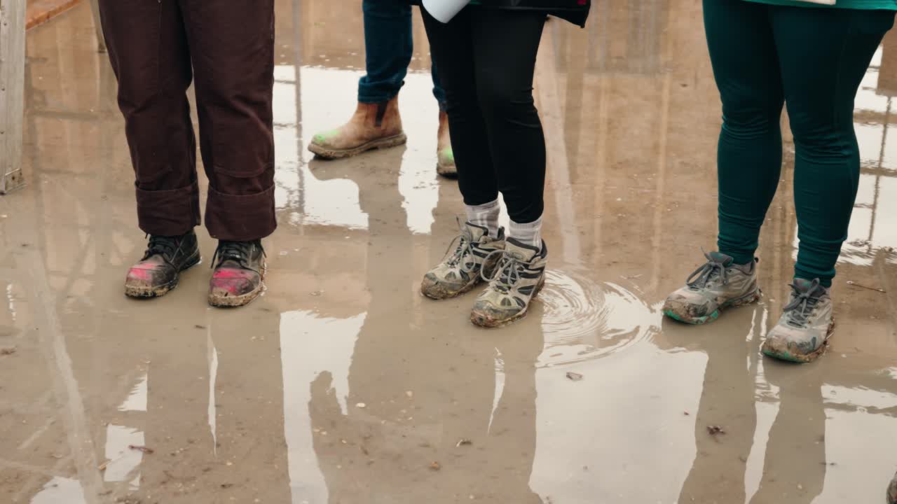 Slow panning shot of workers’ boots and pants inside wet under-construction house