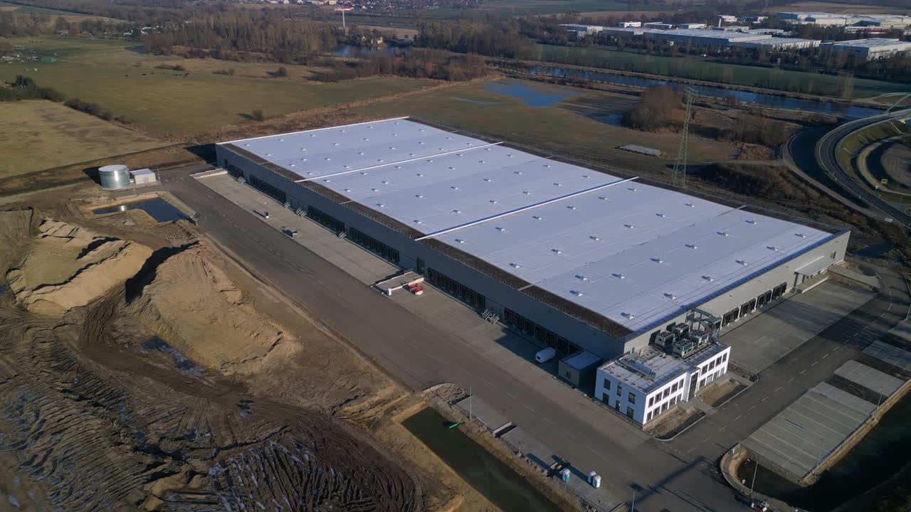 Nuovo grande centro di logistica in costruzione con un'ampia area di stoccaggio, banchine di carico e terreno vuoto circostante. Splendida vista aerea, speed ramp, hyper motion, time lapse, panorama, orbit, drone