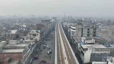 Luftaufnahmen-Entlang-Der-Leeren-Orangefarbenen-U-Bahn-Strecke-In-Lahore-Mit-Dunstiger-Luftverschmutzung-Im-Hintergrund