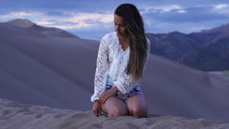 mujer actriz modelo sentada en la cima de colorado las grandes dunas de arena parque nacional reflejando mirando hacia abajo dibujando dedo paisaje de montaña pintoresco crepúsculo aventura púrpura montaña rocosa todavía movimiento
