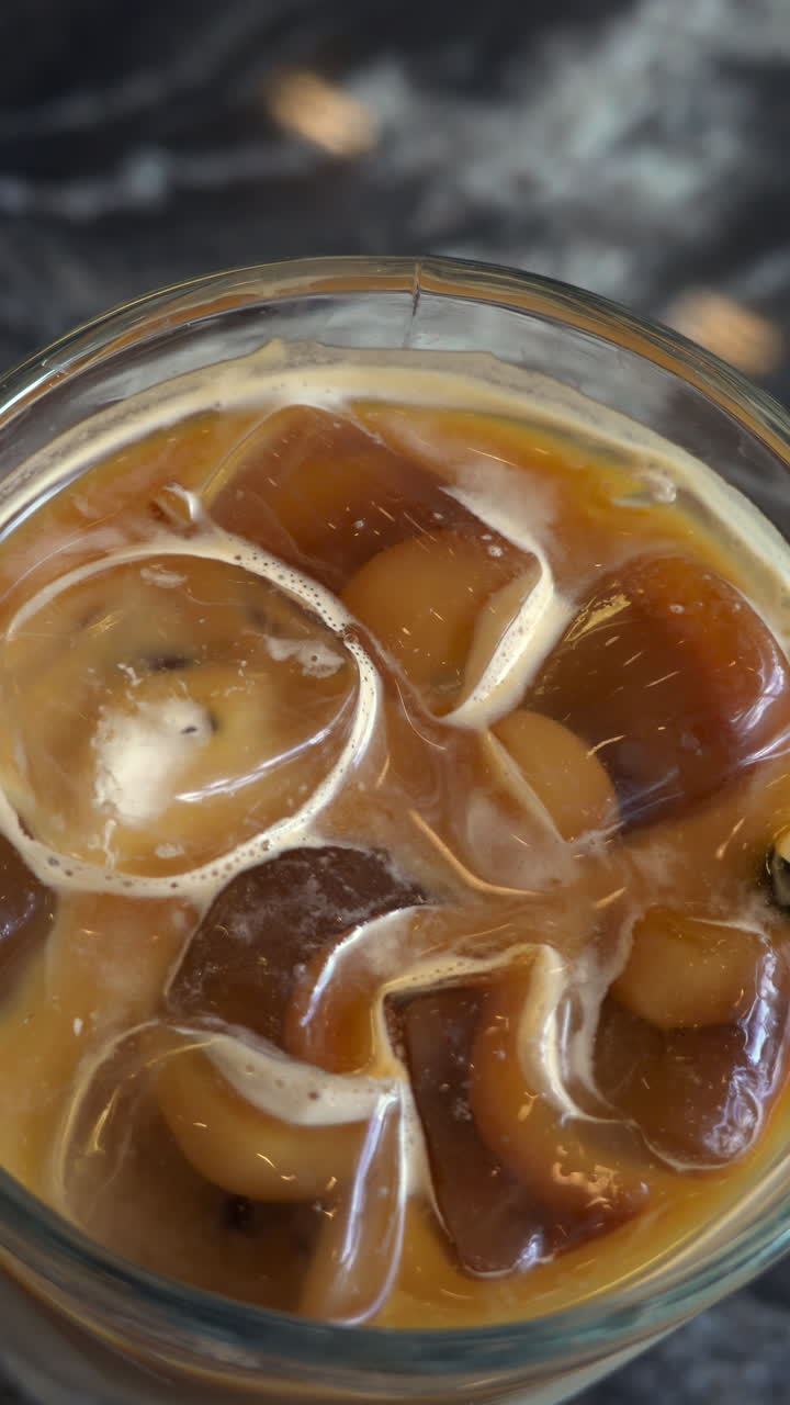 Close up of an iced latte on a black table. Vertical