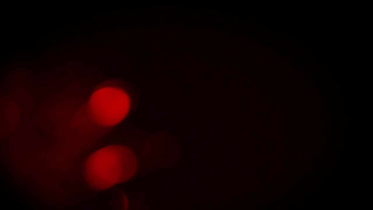 Soft, out-of-focus red bokeh lights and lens flares gently drift and fade on black background. For moody or romantic overlays