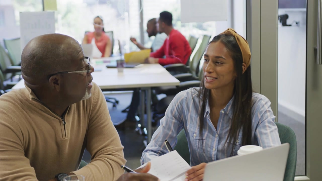 Senior mentoring junior reading docs alerts via laptop rising over faces showing marketing metrics