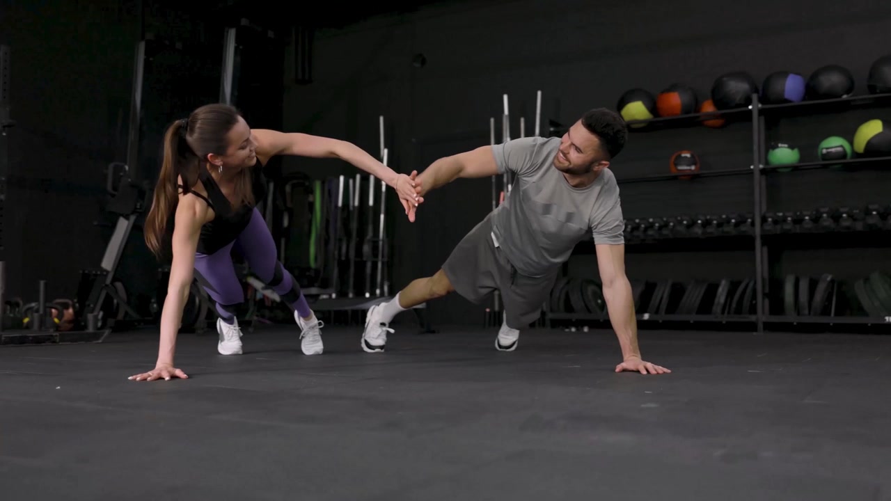 Hombre y mujer chocando las cinco durante flexiones en pareja en el gimnasio