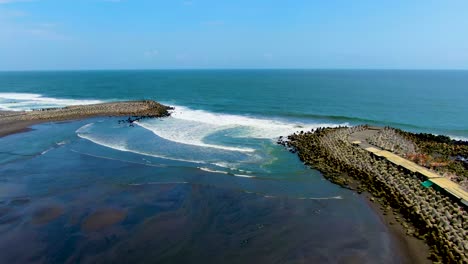 black sand glagah beach lagoon, ocean waves crush on breakwater, java, indonesia