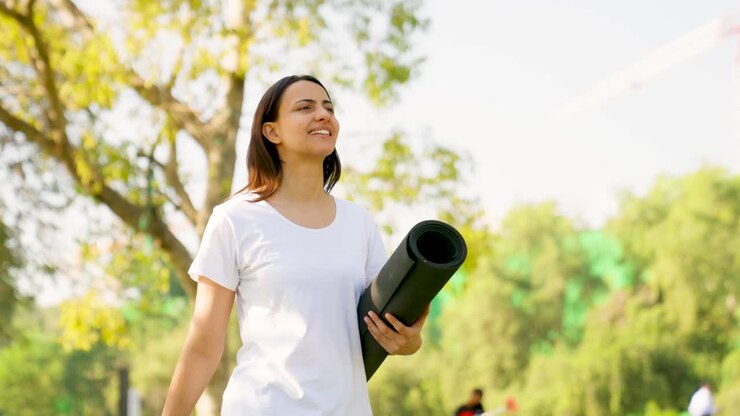 mujer india caminando con un tapete de yoga en un parque por la mañana