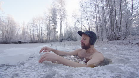 an ice bather enters the ice hole and sits down up to his neck, breathing