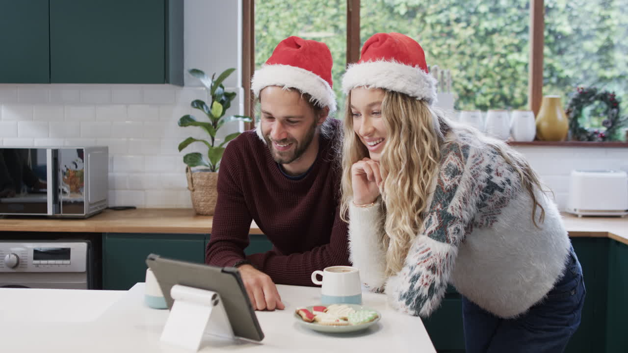 una pareja diversa con sombreros de santa usando una tableta para una llamada de video de navidad, en cámara lenta
