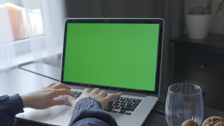 Person am Schreibtisch, tippt mit beiden Händen auf einem Laptop mit grünem Bildschirm.