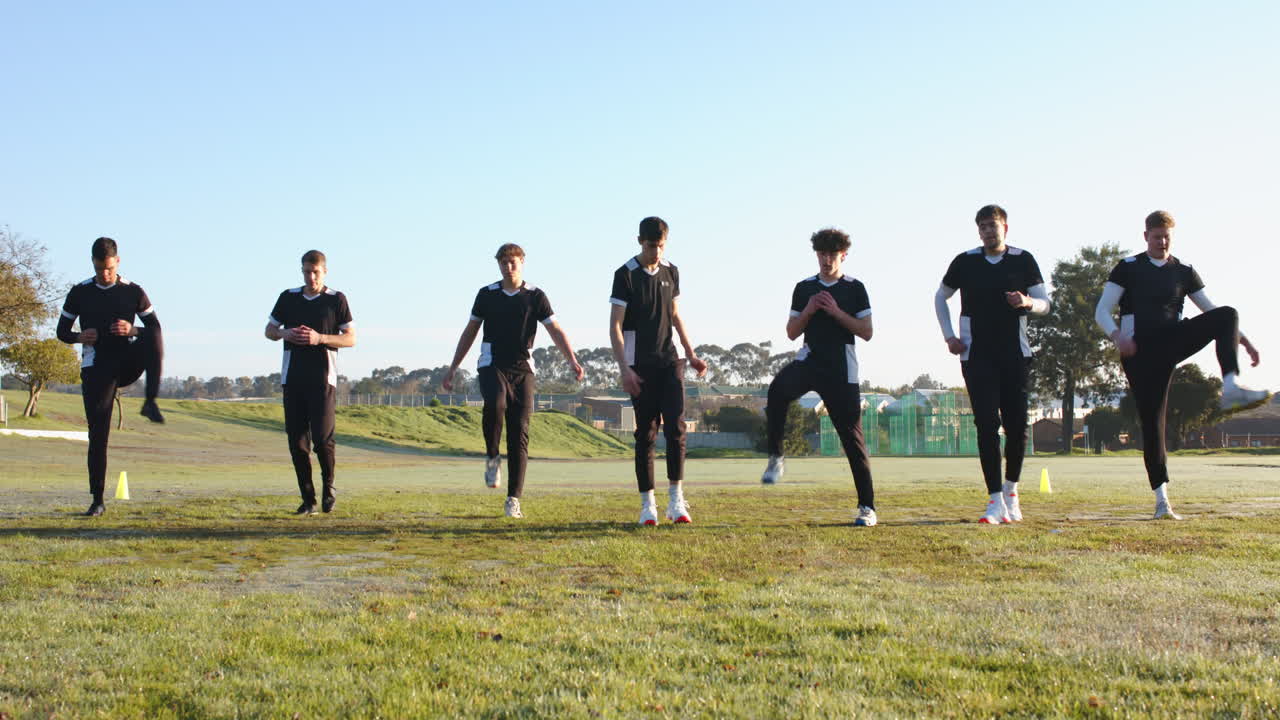 Cricket players warming up on field, performing leg stretches and exercises