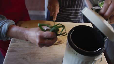 Pareja-Caucásica-Mayor-Usando-Delantales-Y-Cocinando,-Compostando-Esquejes-De-Verduras-En-La-Cocina