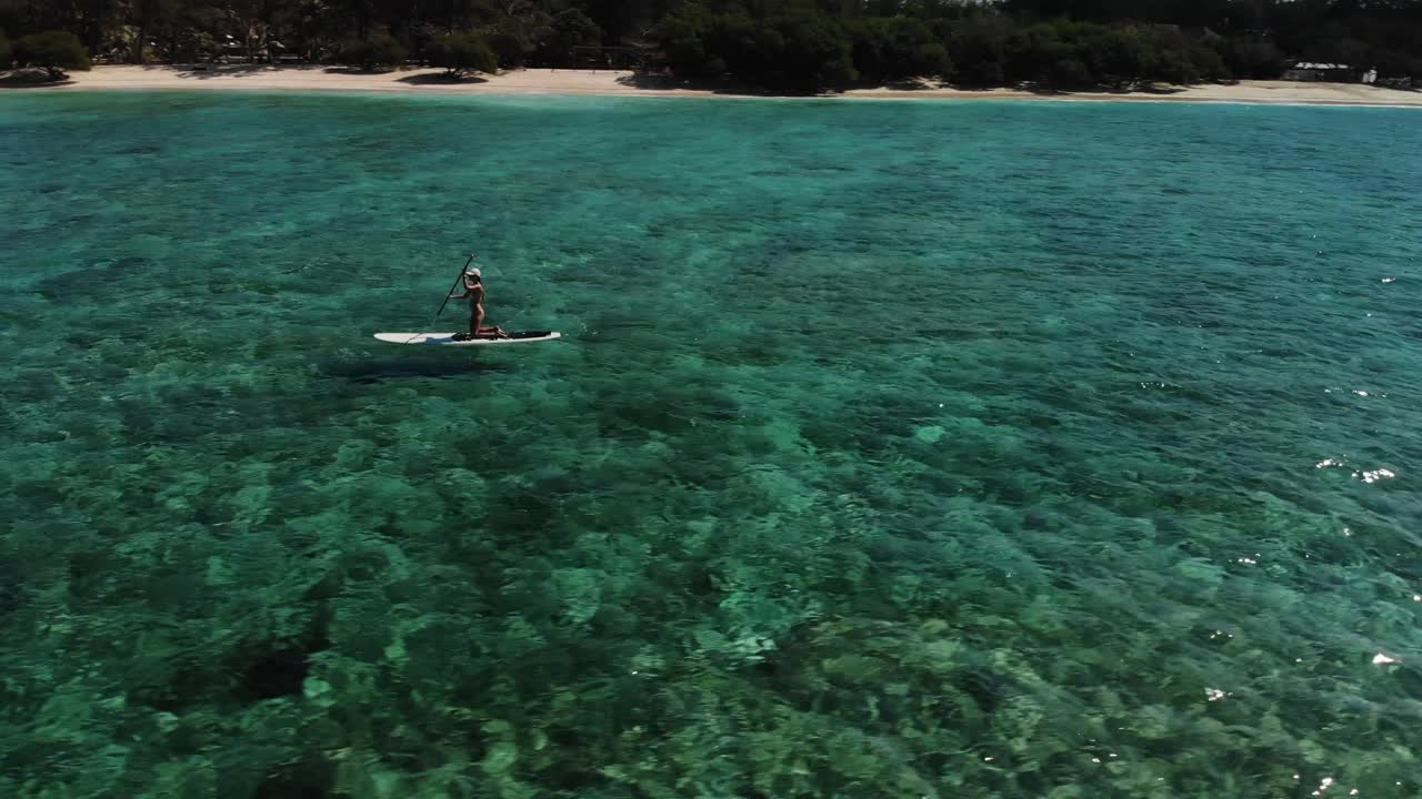 Drone circling around a girl on a paddling board at gili trawangan island, Transparent water and beautiful corals Gili Islands