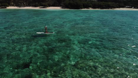 drone circling around a girl on a paddling board at gili trawangan island, transparent water and beautiful corals gili islands