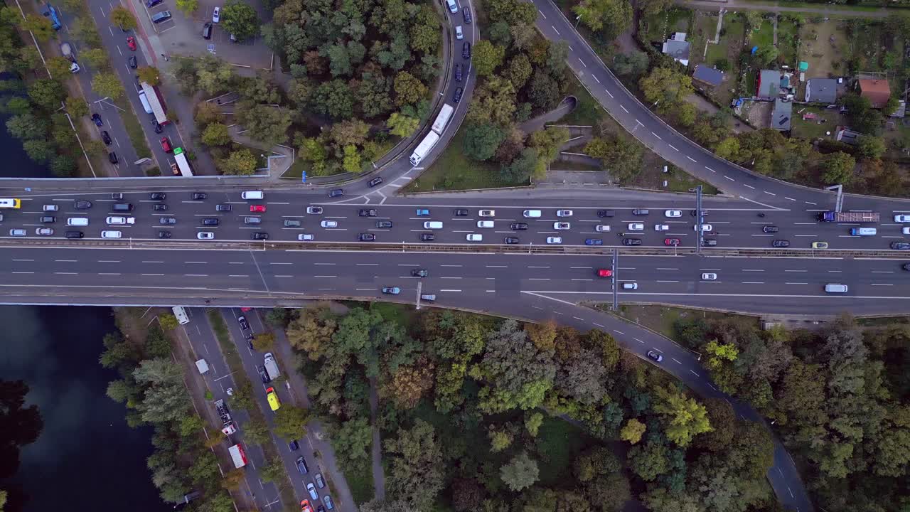 busy highway traffic crossing a bridge over a river surrounded by trees. Dramatic aerial view flight vertical bird's eye view overflight flyover drone