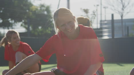 female soccer team warming up with stretches in training against flaring sun