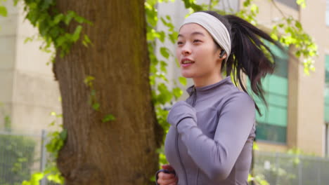무선 이어폰 1을 착용하여 도시 거리를 따라 달리기를 연습하는 젊은 여성의 클로즈업