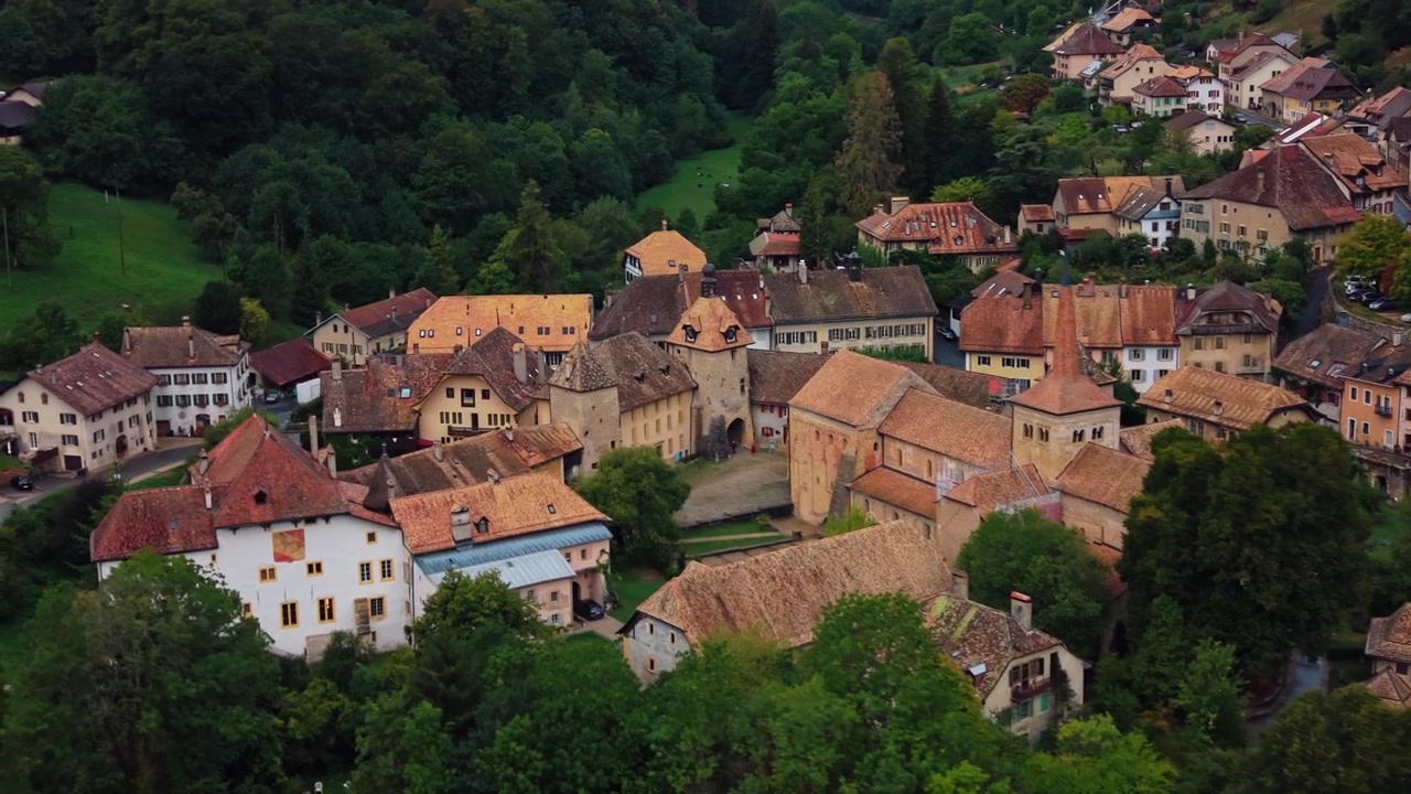 Un drone vola in avanti sopra i tetti di tegole di Romainmotier-Envy, nel Vaud, in Svizzera, con vista sulle case del villaggio, sulla chiesa e sul verde circostante
