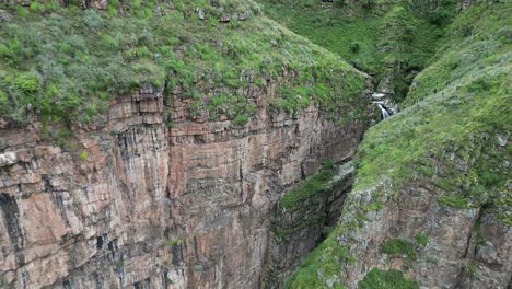 aerial turns at mountain cliff revealing waterfall in tight deep gorge