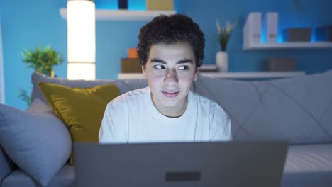 un chico lindo y feliz enviando mensajes de texto en su portátil en casa, navegando por las redes sociales, haciendo amigos virtuales.
