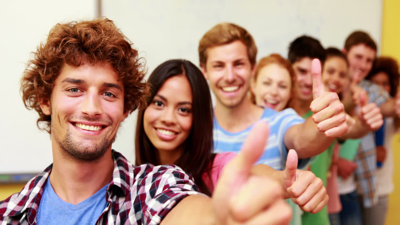 Students standing in classroom giving thumbs to camera in a line