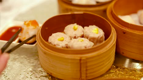 chopsticks pick dim sum from a bamboo steamer in a warmly lit chinese restaurant setting