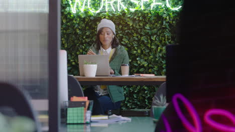 Joven-Mujer-De-Negocios-Afroamericana-Usando-Una-Computadora-Portátil-Viendo-Entretenimiento-En-Línea-Comiendo-Comida-Disfrutando-Del-Almuerzo-Escuchando-Música-En-Un-Lugar-De-Trabajo-De-Oficina-Moderno