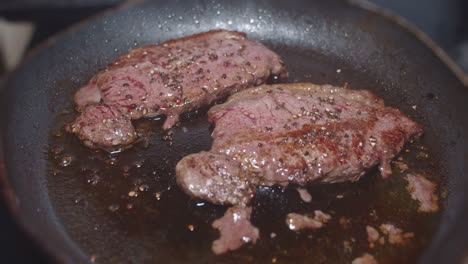 thin steaks cooking in oil in skillet and being turned with spatula