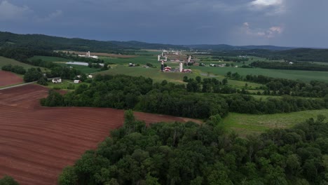Aerial flyover yellow and red cultivated farm fields in American countryside. Farmsteads in distance. Cloudy summer day in Pennsylvania. Wide shot