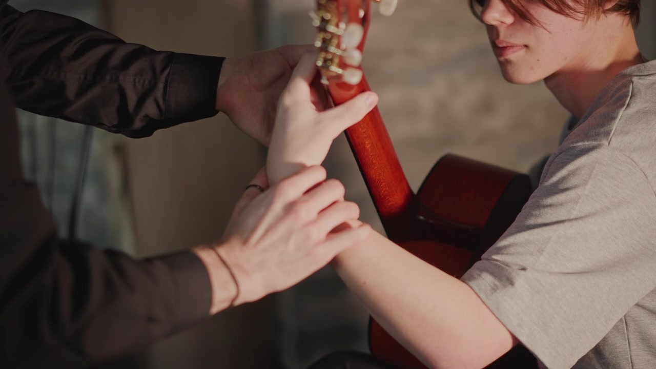 Instructor assists student. Mentor helps tune guitar. Educational session with careful instrument adjustment. Teacher patiently guides student through guitar tuning process in studio