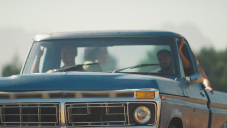 two women riding in back of pick up truck as friends arrive at countryside cabin on road trip