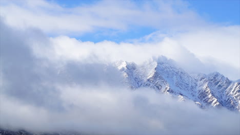 clouds moving over the with snow covered mountain peaks while the sun is shining