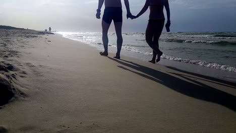 hombre y mujer caminando en la playa de arena tomados de la mano